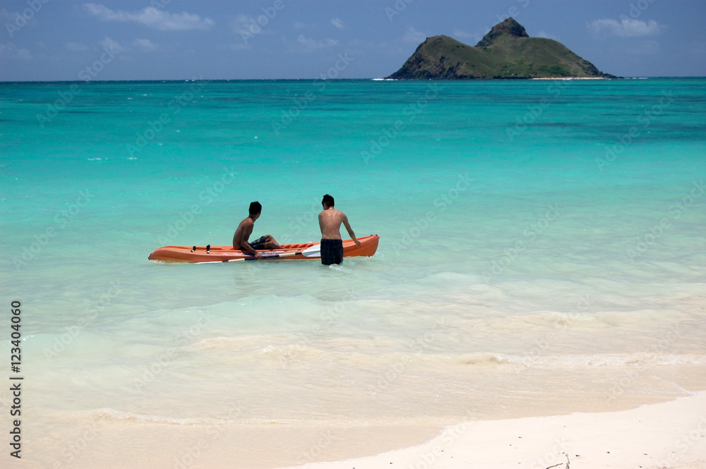 Young boys jumping into a kayak on the turquoise ocean of Lanikai beach, with island at the horizon, Oahu, Hawaii
