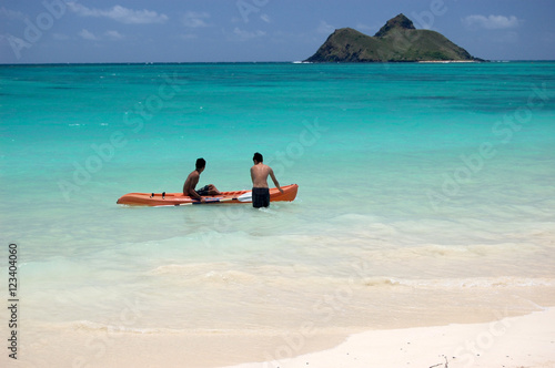 Young boys jumping into a kayak on the turquoise ocean of Lanikai beach, with island at the horizon, Oahu, Hawaii © mhgstan