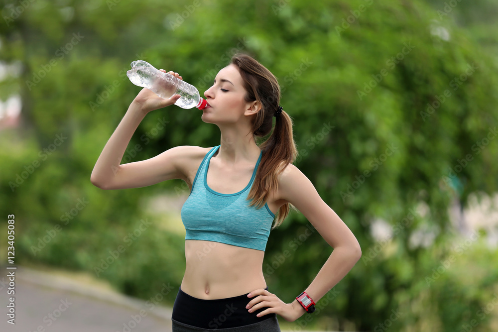 Young woman drinking water after run in park Young woman drinking water after run in park