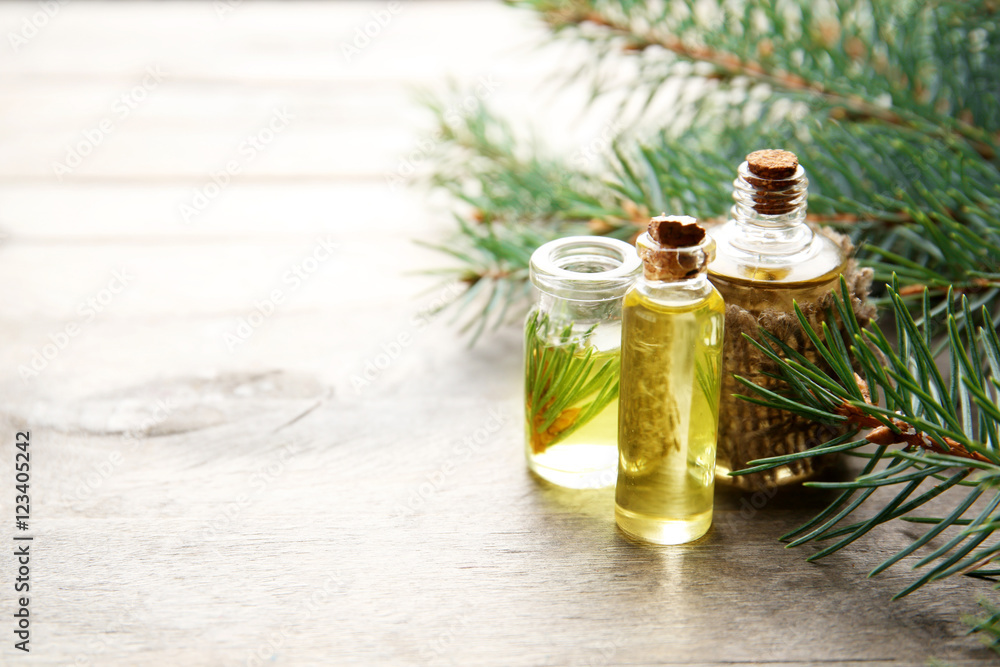 Bottles of coniferous essential oil and branches on wooden background, close up view Bottles of coniferous essential oil and branches on wooden background, close up view
