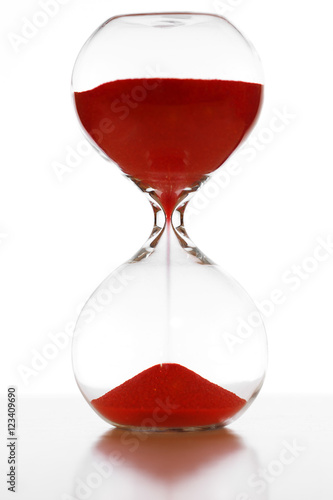 Glass hourglass with red sand running through measuring passing