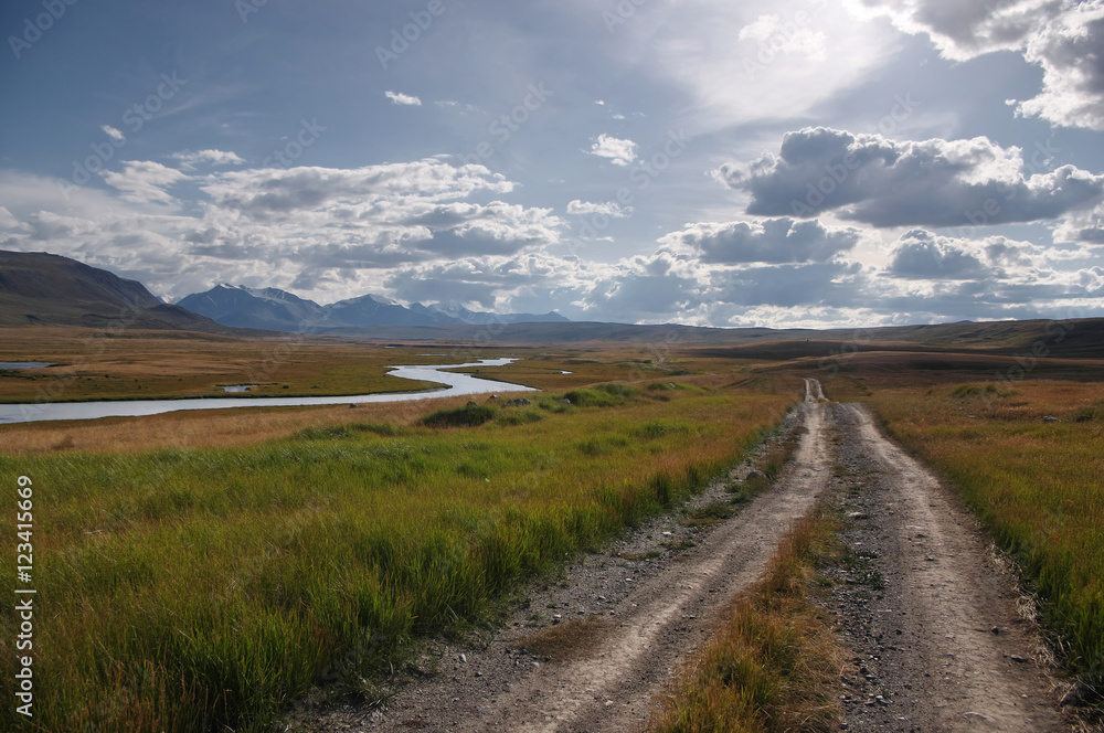 Road on a mountain plateau with the orange grass at the background of the valley of white river under a blue sky with white clouds, Plateau Ukok, Altai mountains, Siberia, Russia