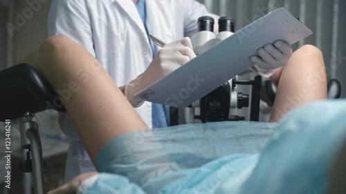 Over the shoulder shot of woman lying on gynecological chair and being examined by female doctor with colposcopy microscope  photo