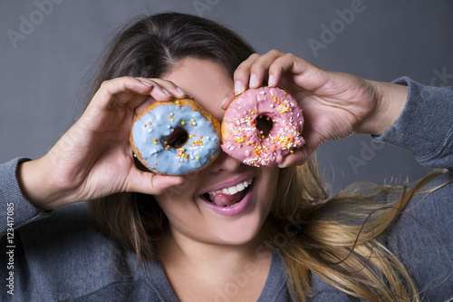 Happy beautiful young caucasian plus size model posing with donuts on a gray studio background