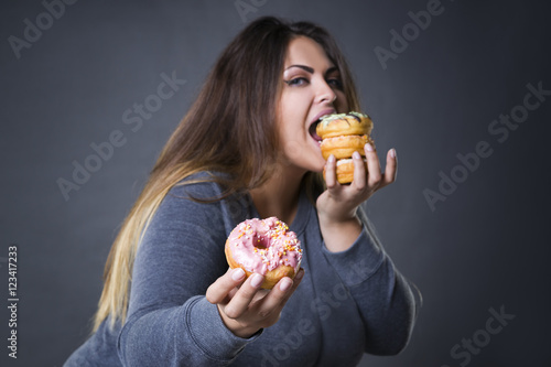 Принти на полотні Happy beautiful young caucasian plus size model posing with donuts on a gray stu