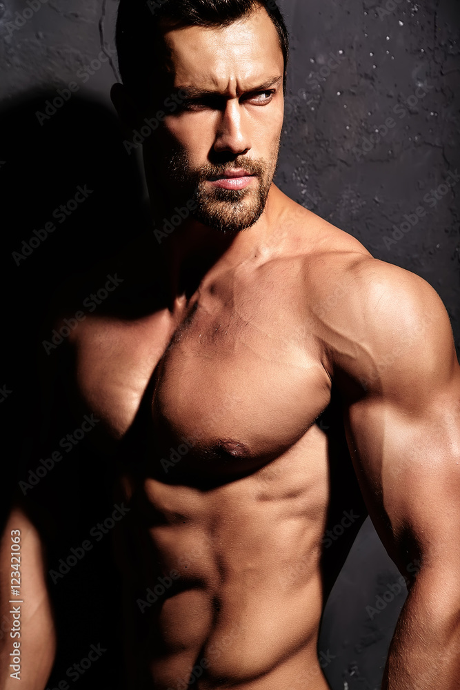 Fototapeta premium Portrait of strong healthy handsome Athletic Man Fitness Model posing near dark gray wall