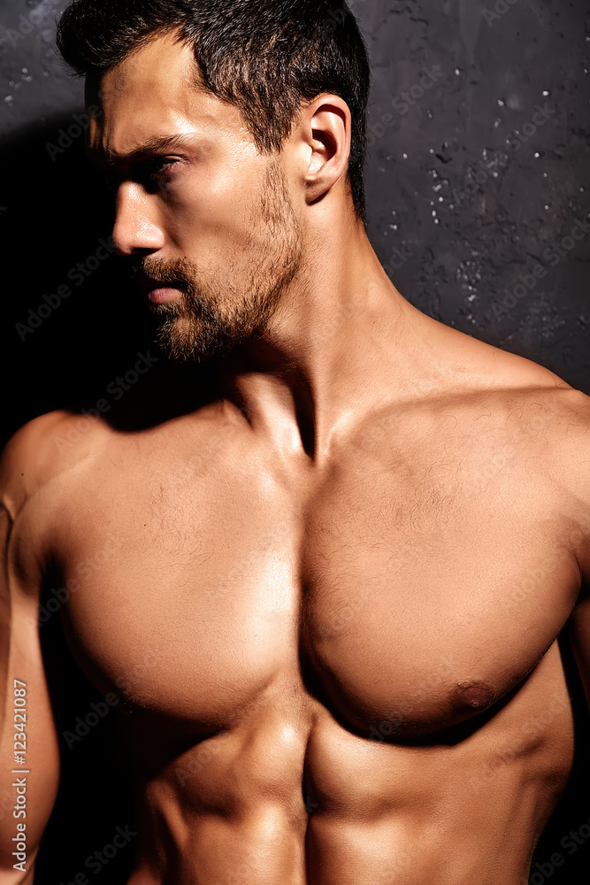 Portrait of strong healthy handsome Athletic Man Fitness Model posing near dark gray wall