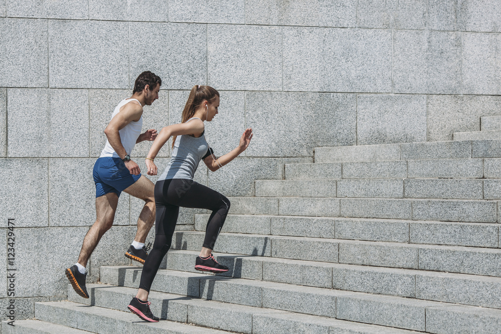 Determined friends jogging up steps by wall Determined friends jogging up steps by wall