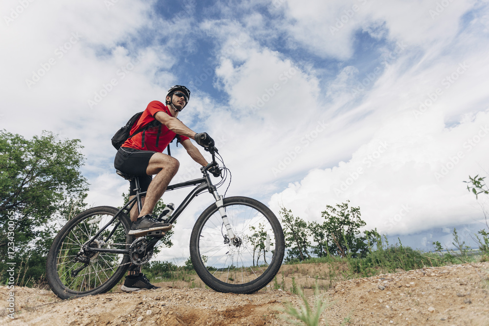 Low angle view of man riding mountain bike in rural setting against sky Low angle view of man riding mountain bike in rural setting against sky