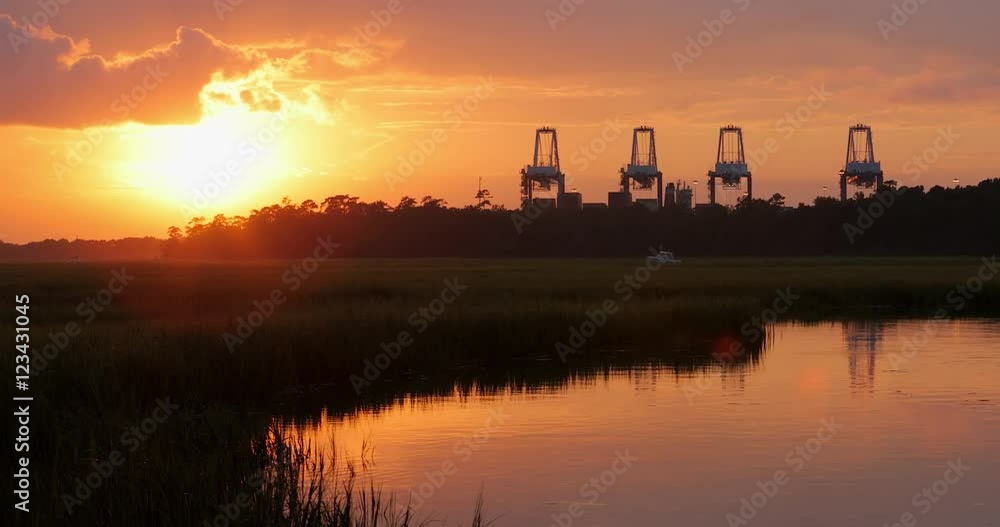 A marsh at sunset with industrial ship loading cranes in view along with boats and water. A marsh at sunset with industrial ship loading cranes in view along with boats and water.