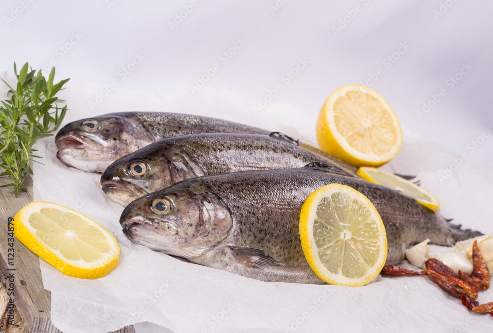 Three raw trouts on paper with thyme and lemon on a rustic wooden table Three raw trouts on paper with thyme and lemon on a rustic wooden table