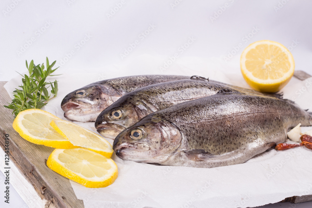 Three raw trouts on paper with thyme and lemon on a rustic wooden table Three raw trouts on paper with thyme and lemon on a rustic wooden table