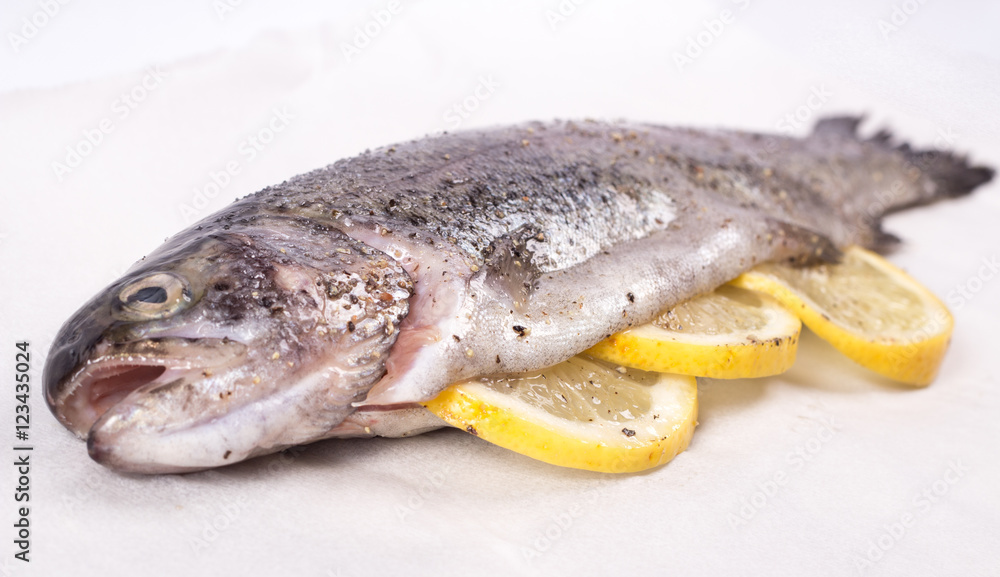Three raw trouts on paper with thyme and lemon on a rustic wooden table Three raw trouts on paper with thyme and lemon on a rustic wooden table