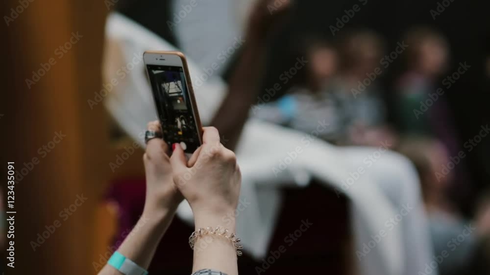 Closeup hands of a girl holding smartphone and taking pictures of a fashion show Closeup hands of a girl holding smartphone and taking pictures of a fashion show