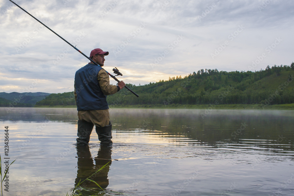 Man holding fishing rod while standing in river against sky Man holding fishing rod while standing in river against sky