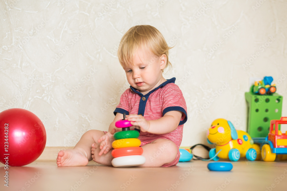 1,5 year-old child playing with educational cup toys at home. Little blond baby boy with blue eyes is playing with pyramid toy on the floor. Little kid have fun indoors 1,5 year-old child playing with educational cup toys at home. Little blond baby boy with blue eyes is playing with pyramid toy on the floor. Little kid have fun indoors