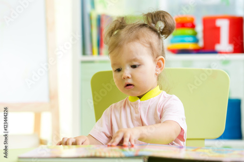 cute baby girl reads a book at home