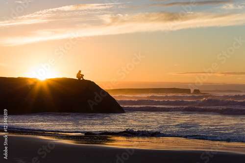 a man is sitting on the rock enjoying breathtaking ocean view at sunset 
