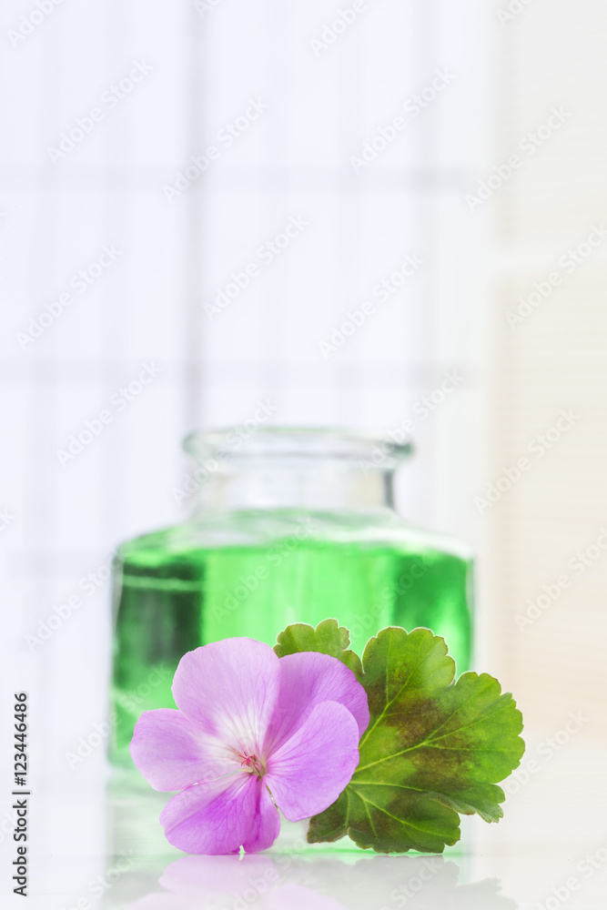 Pink geranium flower with an aromatherapy essential oil glass bottle,