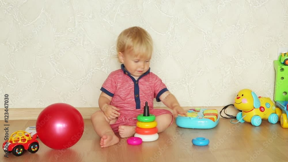 1,5 year-old child playing with educational cup toys at home. Little blond baby boy with blue eyes is playing with pyramid toy on the floor. Little kid have fun indoors 1,5 year-old child playing with educational cup toys at home. Little blond baby boy with blue eyes is playing with pyramid toy on the floor. Little kid have fun indoors