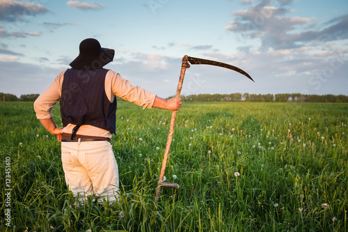 Farmer with a scythe on green field photo