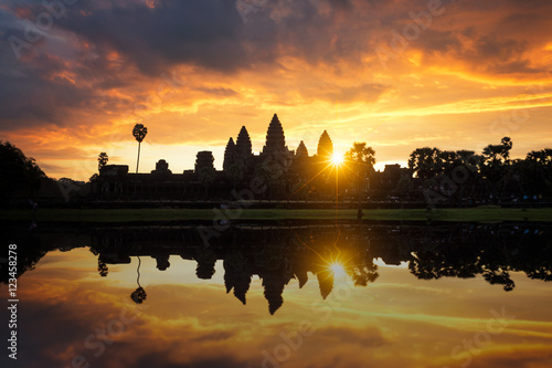 Towers of ancient temple complex Angkor Wat at sunrise. Siem Reap, Cambodia. Temple Mountain and the sun reflected in lake at dawn. Mysterious Angkor Wat is a popular tourist attraction. © weerasak