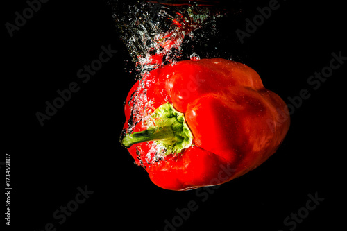 Red bell pepper falling and splashing into the water on black background.