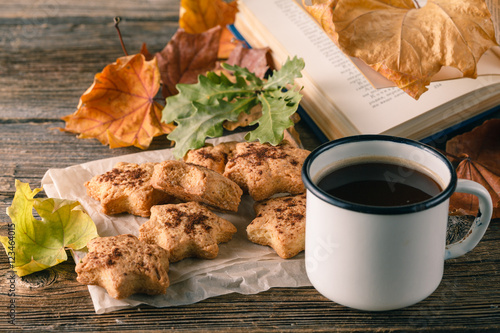 Cup of tea with old book, autumn leaves on wooden table. photo