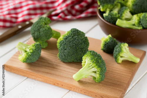 Broccoli scattered on cutting board and in a brown bowl.