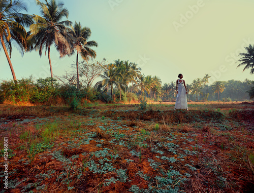 Woman wearing white dress standing in field by palm trees