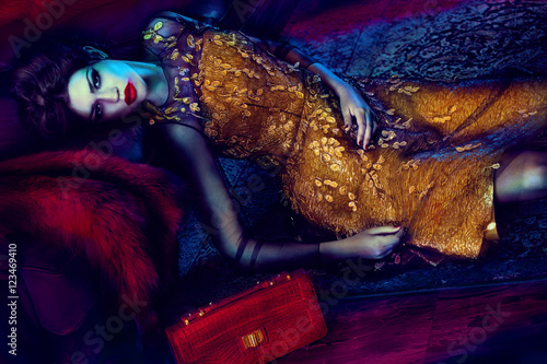 Woman in gold dress lying down with red handbag  (ID: 123469410)