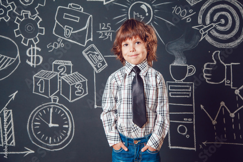 Little boy as businessman or teacher wearing shirt and tie on a dark background with business school picture © kanashkin