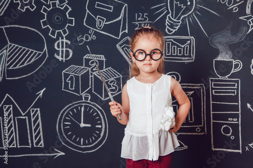 The little smart girl in glasses holding a pointer on dark background with business or school picture © kanashkin