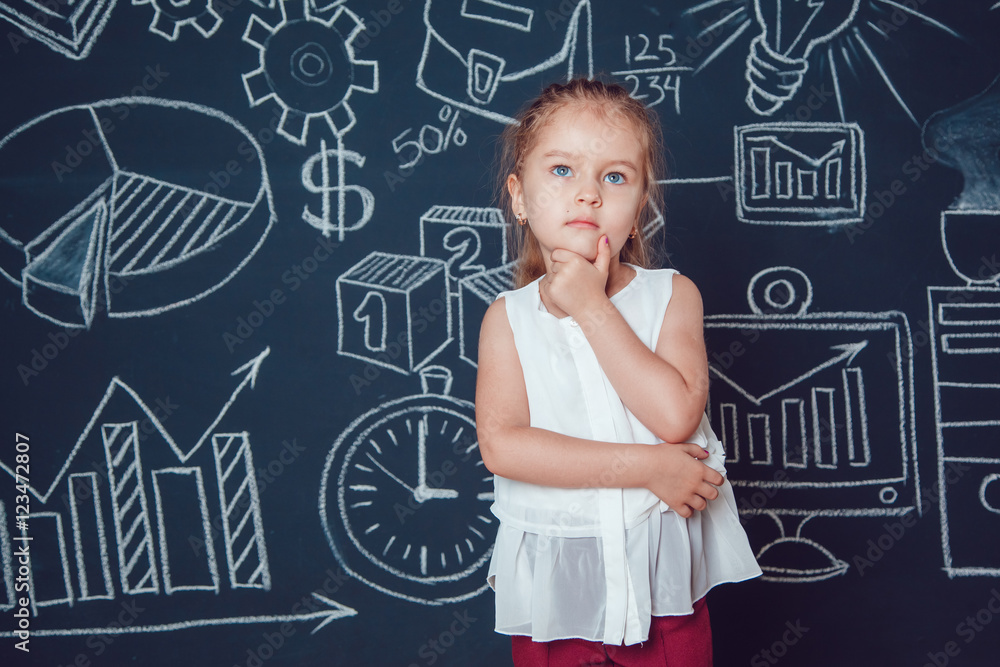 The little smart girl holding her chin on a background of wall with business or school picture The little smart girl holding her chin on a background of wall with business or school picture