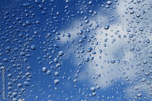 Rain drops on window with blue cloudy sky in background , spring rainy day