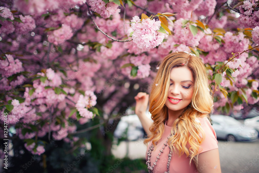 Young beautiful blonde girl with long hair in a pink dress near the cherry trees