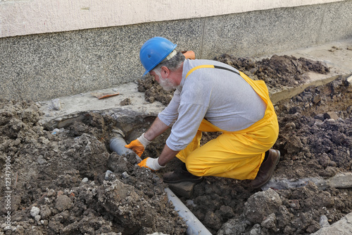 Plumber at construction site installing sewerage tube photo