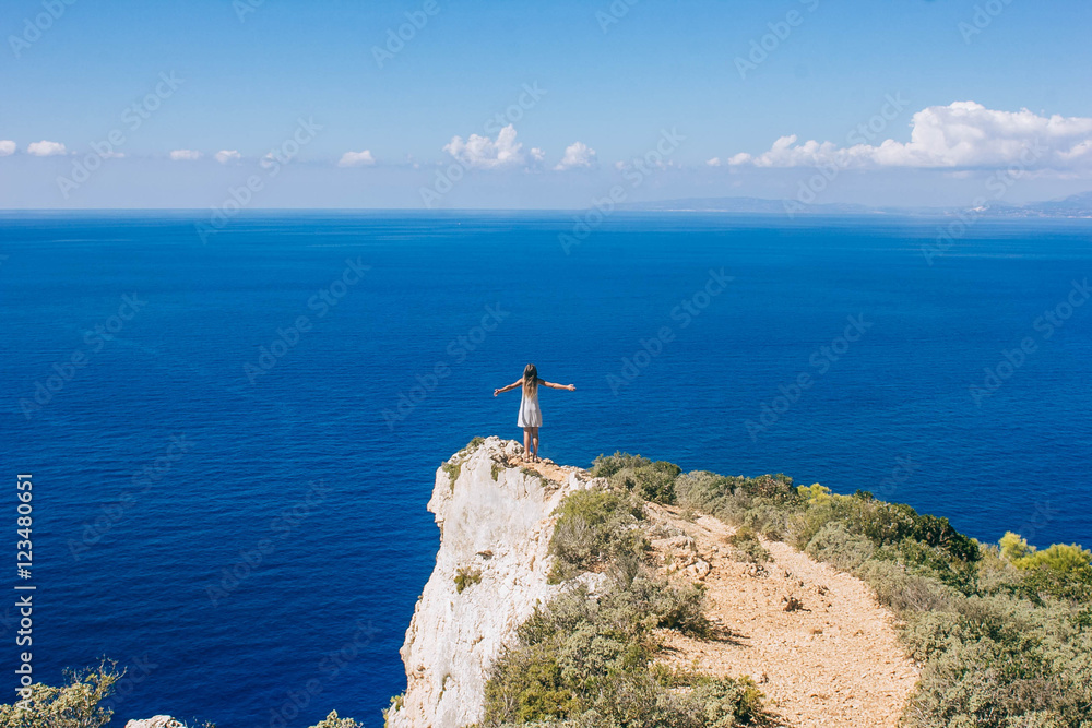 Young girl standing near sea with raised hands
