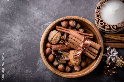 Spices and nuts in wooden bowl on dark background.