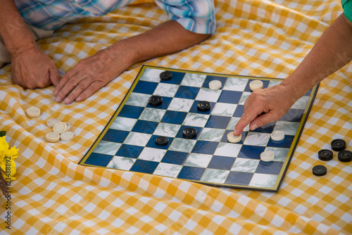 Hands of seniors playing checkers. Checkered yellow cloth. Game for smart people. Attention and logic.