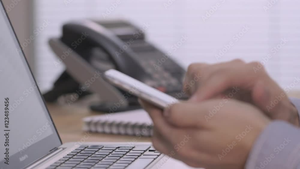 Businessman answering a desk phone while typing on smartphone in a modern office Businessman answering a desk phone while typing on smartphone in a modern office