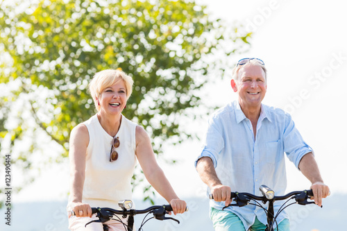 Senioren, Paar aus Frau und Mann, fährt Fahrrad an einem Sonnenblumen Feld © Kzenon