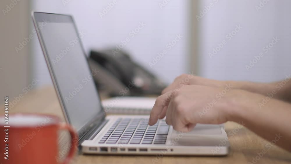 A man finger typing fast on a silver laptop, modern office background A man finger typing fast on a silver laptop, modern office background