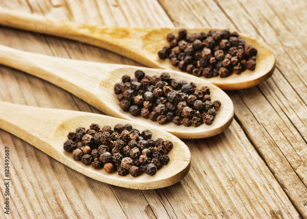 Black pepper in wooden spoon on the old board Black pepper in wooden spoon on the old board