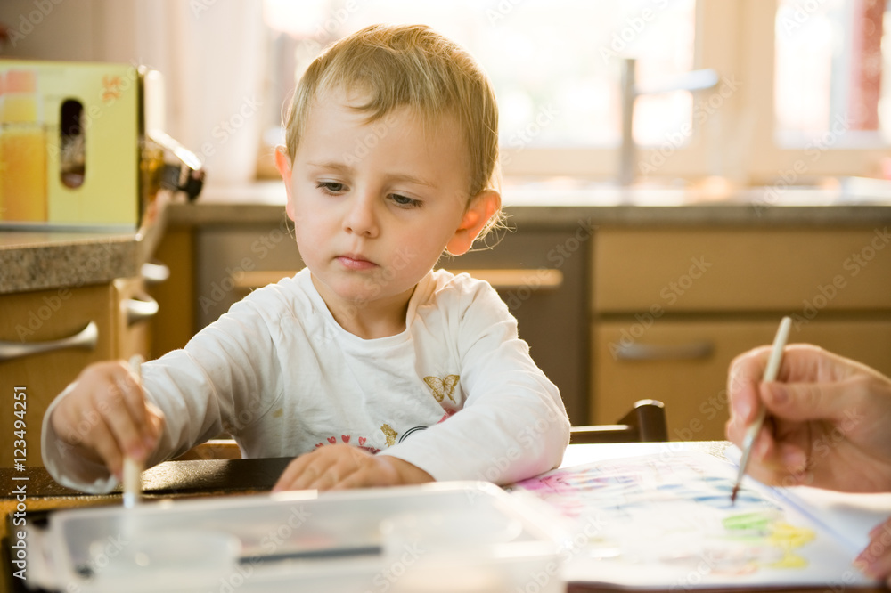 Little girl painting with watercolor at home in the kitchen with her mom Little girl painting with watercolor at home in the kitchen with her mom