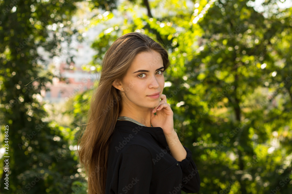Young woman standing sidewise on the background of trees Young woman standing sidewise on the background of trees