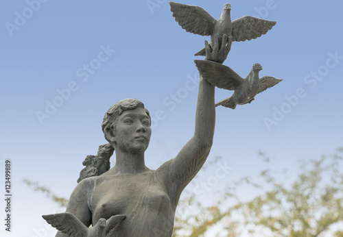 Kyoto, Japan - September 15, 2016: Gray peace statue of girl releasing three doves against blue sky. Statue at the bridge on Nijo Dori over the canal. © Klodien