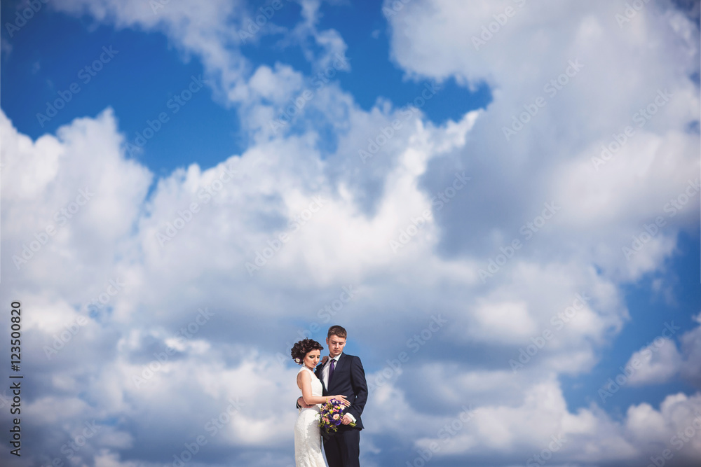 Wedding day. Bride and groom looking at the wedding bouquet on a background of blue sky and white clouds Wedding day. Bride and groom looking at the wedding bouquet on a background of blue sky and white clouds