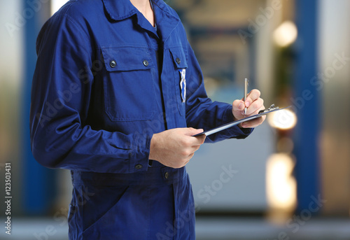 Canvas Print Mechanic in uniform with a clipboard and pen on gas station blurred background