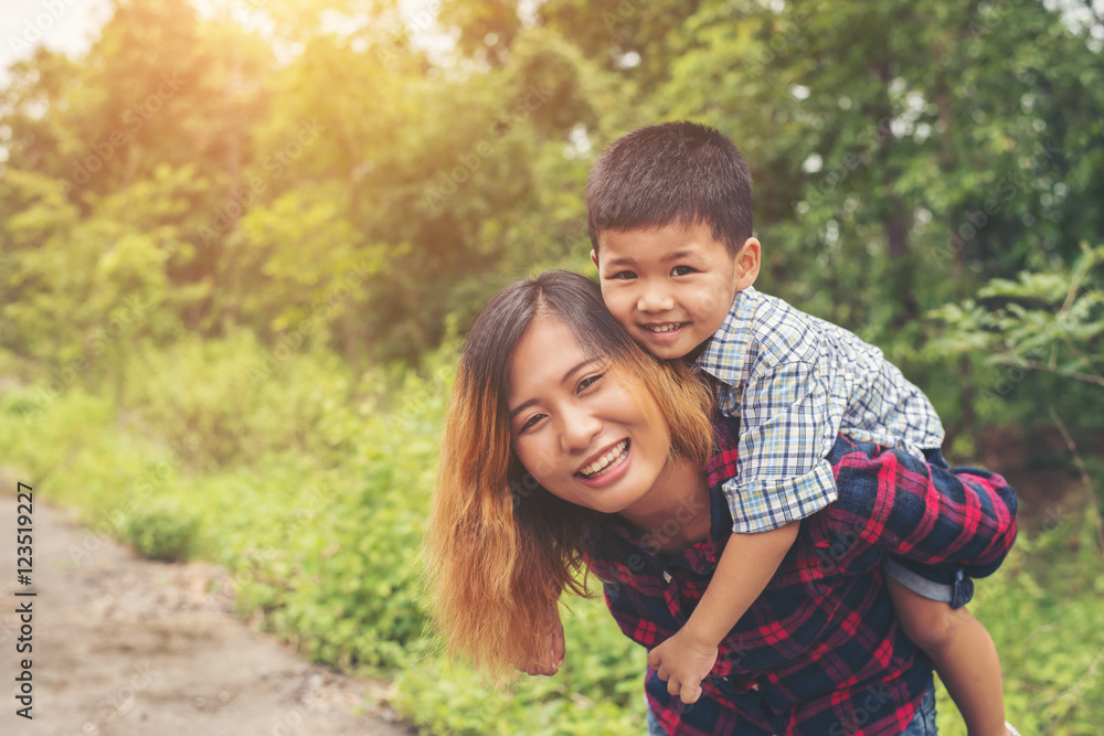 Happy little cute asian boy enjoying a piggyback ride on his mot Happy little cute asian boy enjoying a piggyback ride on his mot